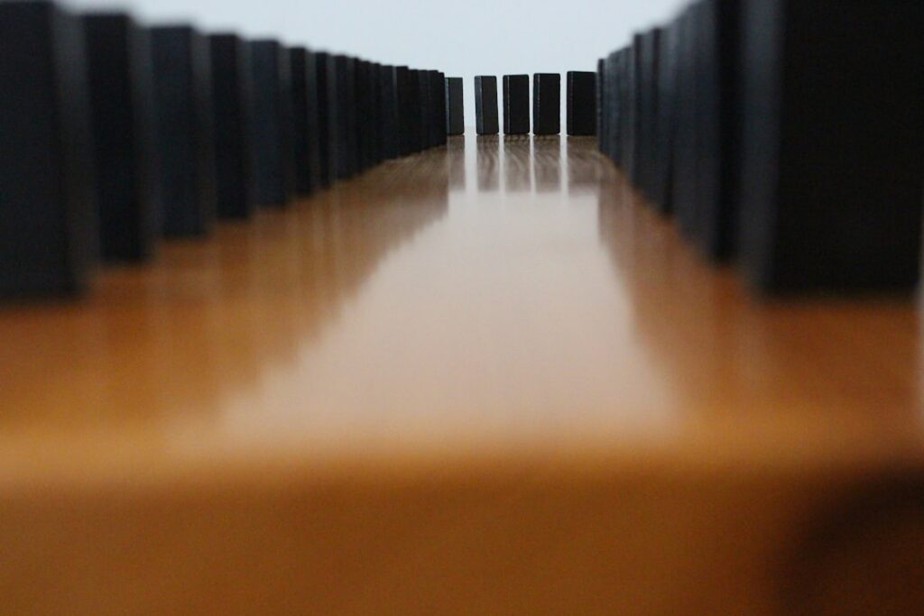 Line of standing white dominos with one falling, starting a chain reaction on a clean, bright background, symbolizing a sm...