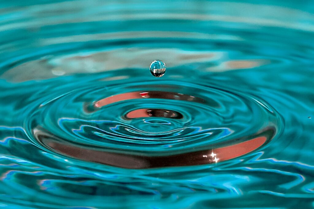 Close-up, high-speed photograph of a single water droplet hitting a calm surface, creating a series of perfect, expanding ...